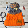 LM WOOLLY HAT Orange and gray knit beanie with brand labels on a wooden surface