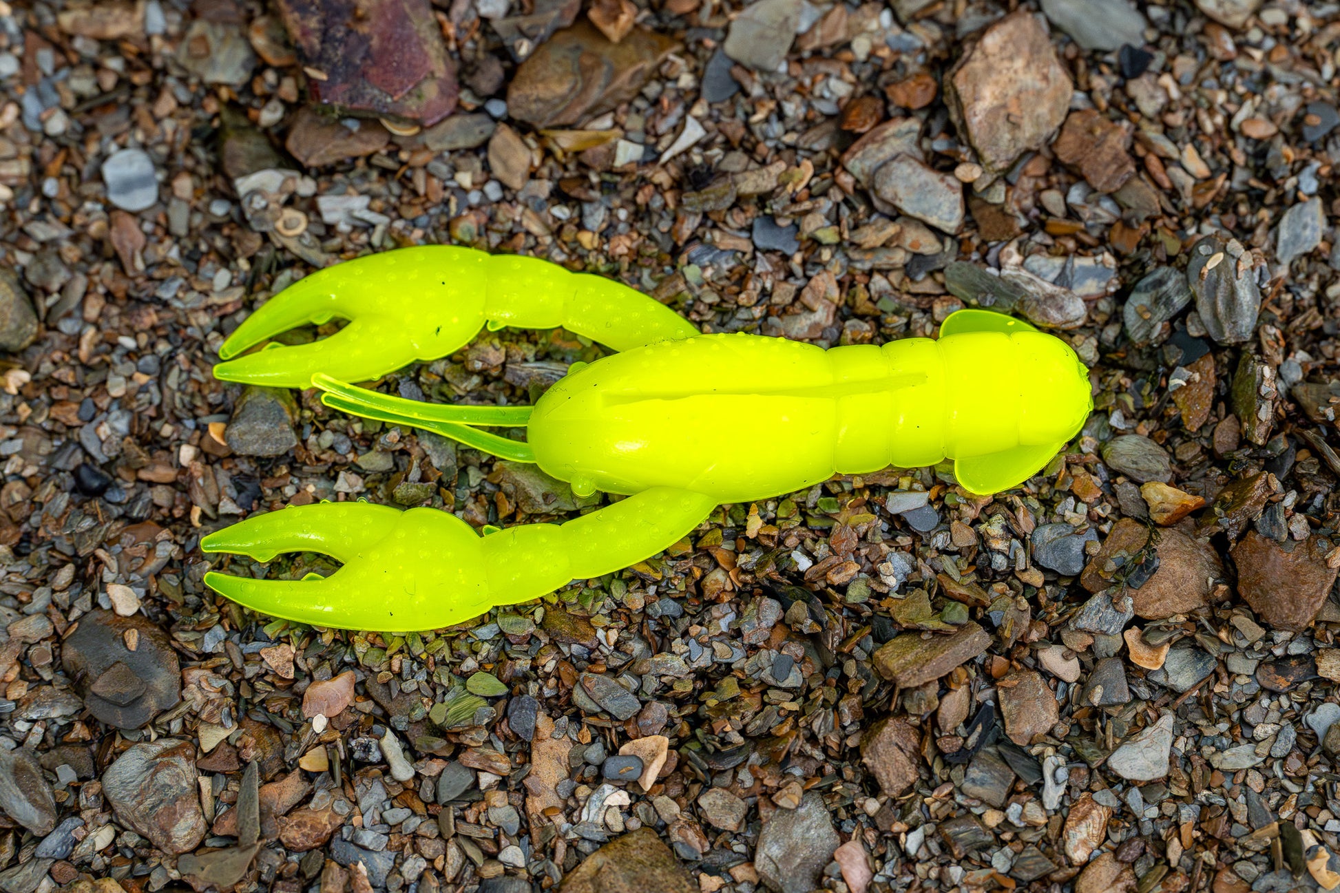 Bright yellow crawfish-shaped fishing lures on a gravel surface