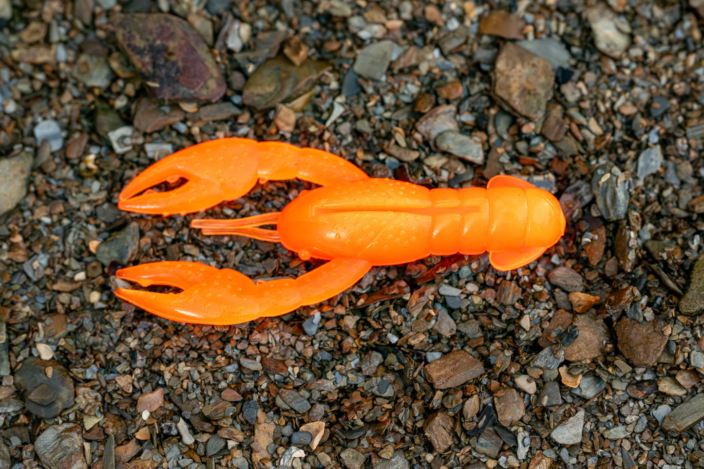 Orange plastic crawfish lure on a gravel surface