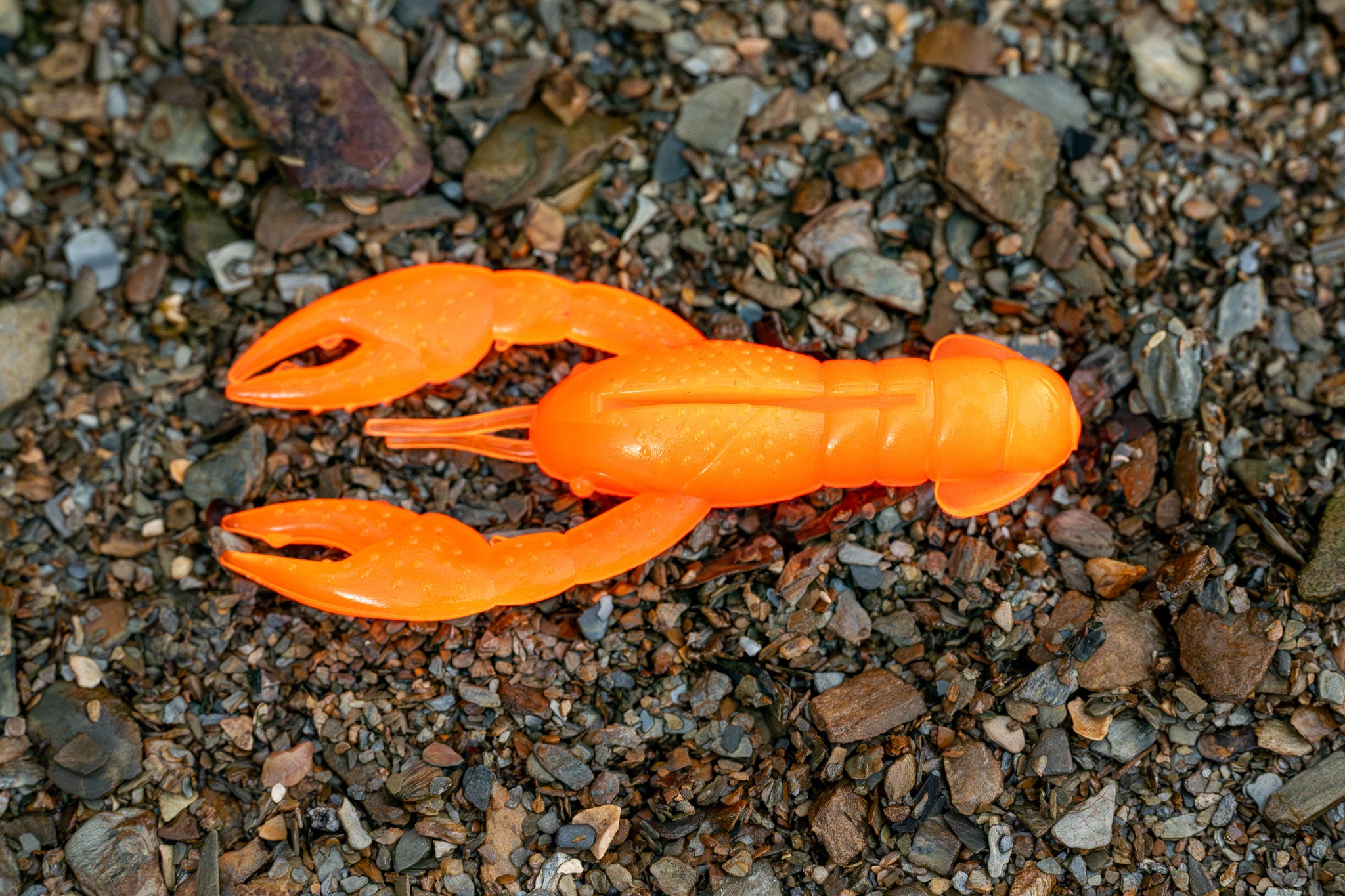 Orange plastic crawfish lure on a gravel surface