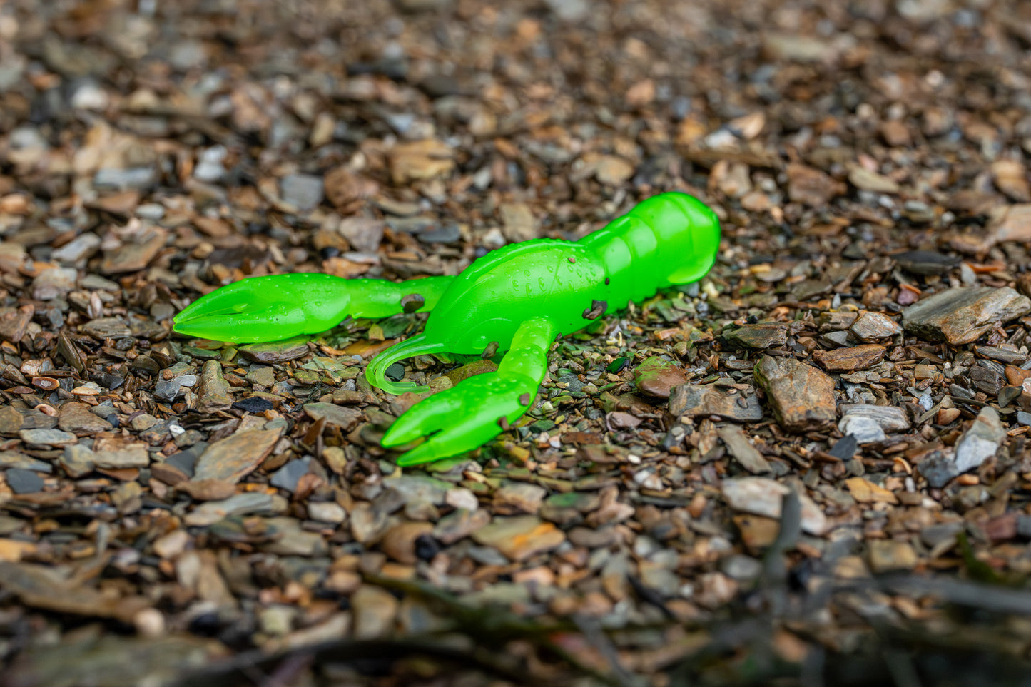 Green plastic crawfish toy on a gravel surface