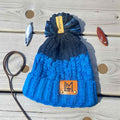LM WOOLLY HAT Blue knit beanie with pom-pom on a wooden surface