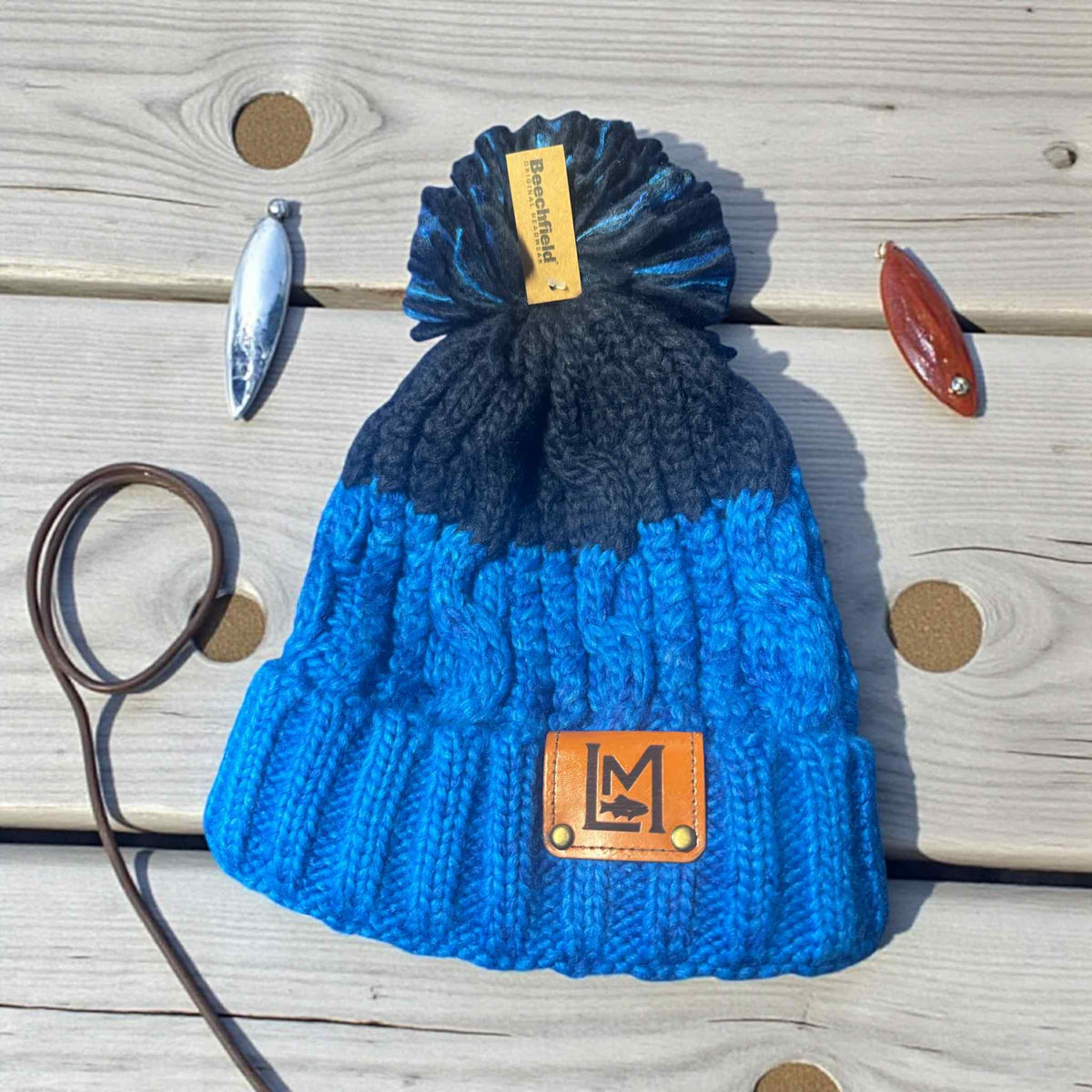 LM WOOLLY HAT Blue knit beanie with pom-pom on a wooden surface